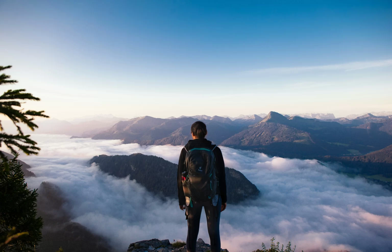 Explorer standing at the top of a mountain looking out over a beautiful cloudy view.  