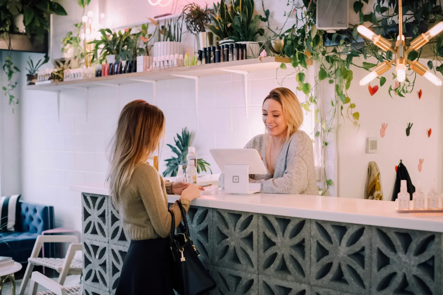 : Smiling woman behind a counter at a store, helping a customer with a purchase. 