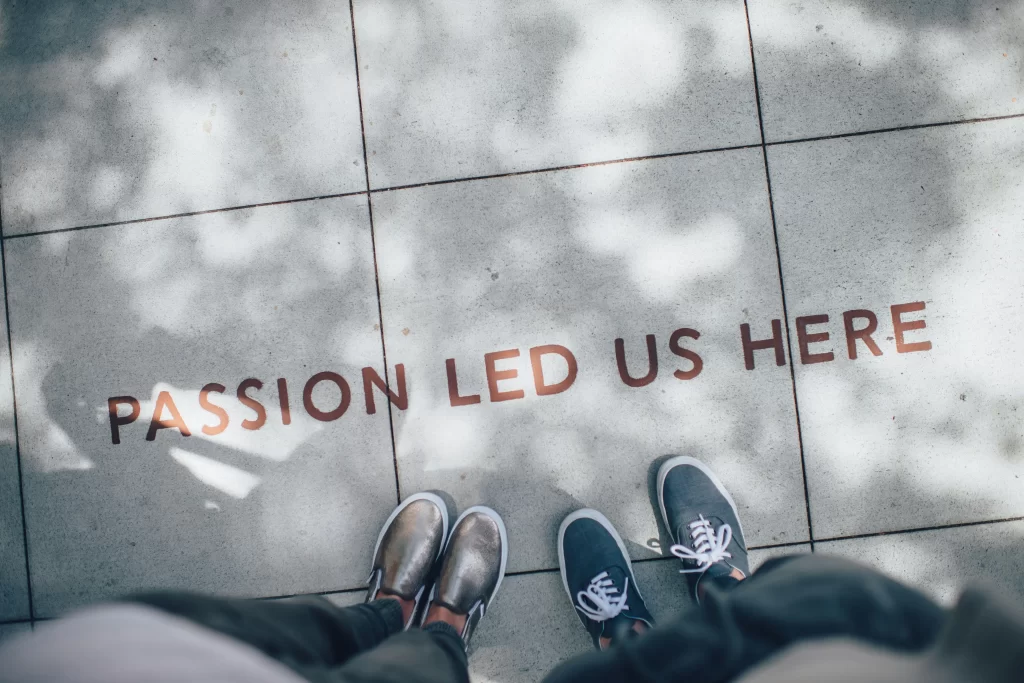 Two people standing over a message etched in the pavement reading “passion led us here”.  