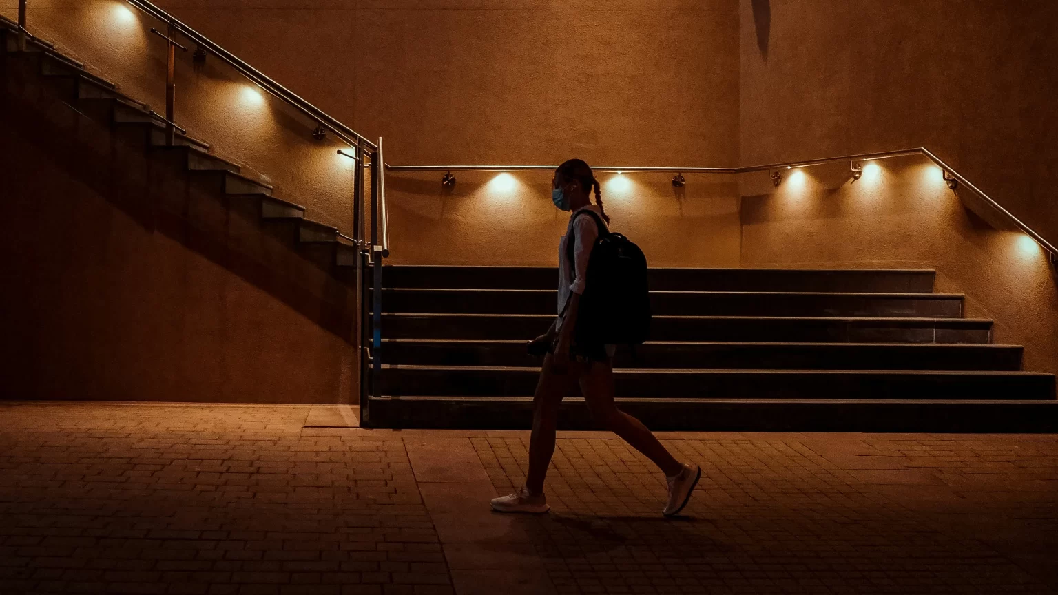 Person walking alone next to a underlit stairwell.  