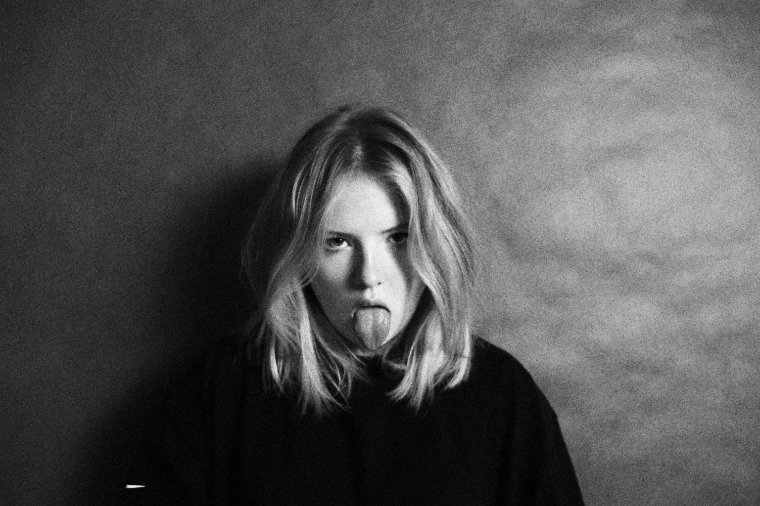 Rebel woman standing on a grey background sticking her tongue out in a defiant manner.  