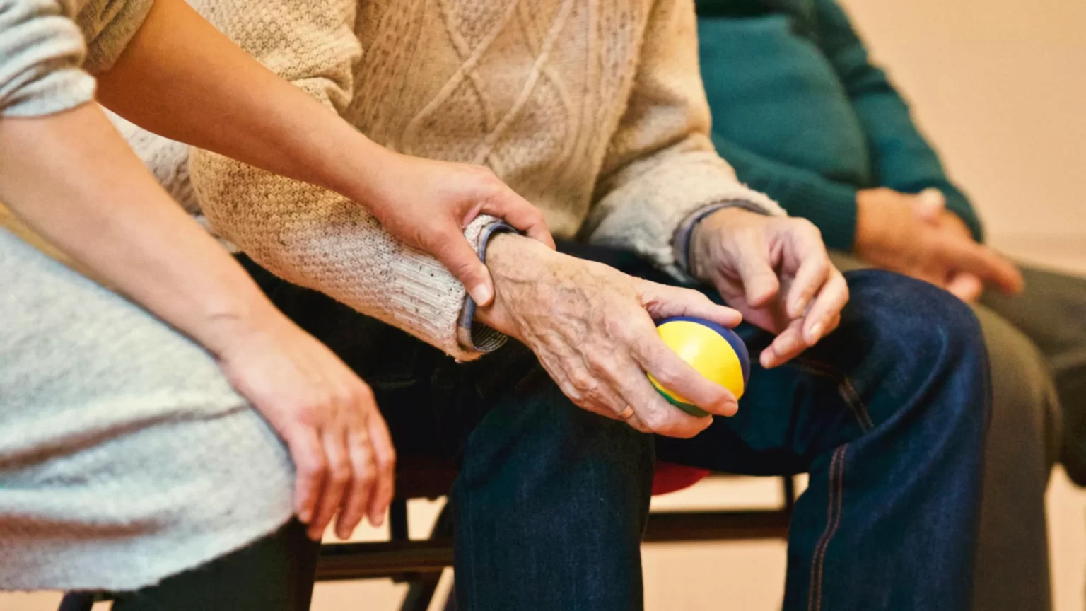 Two people sitting side by side and one caregiver holding an elderly persons hand. 