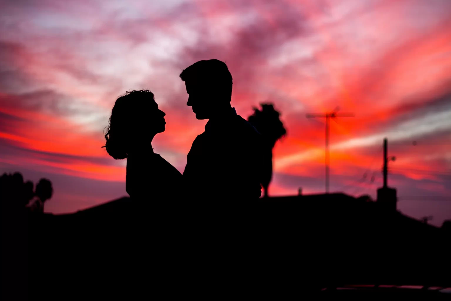 The silhouette of two lovers standing in front of a sunset.  