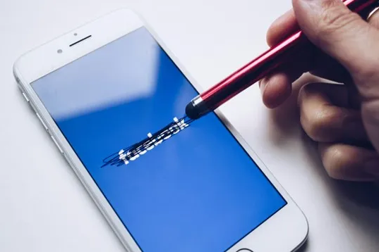 person scratching out the Facebook logo on their phone screen with a stylus. 