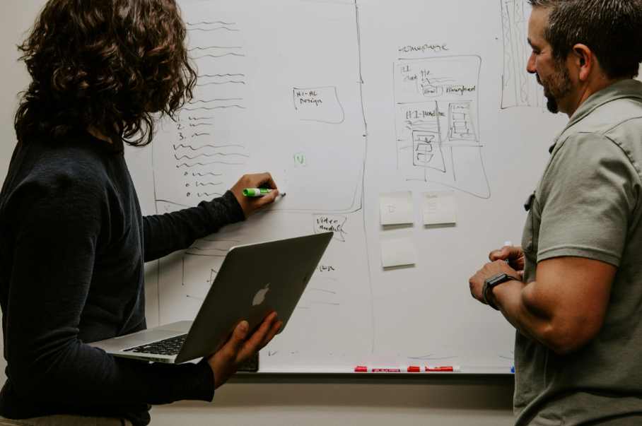 Two people in front of a whiteboard writing out plans. 