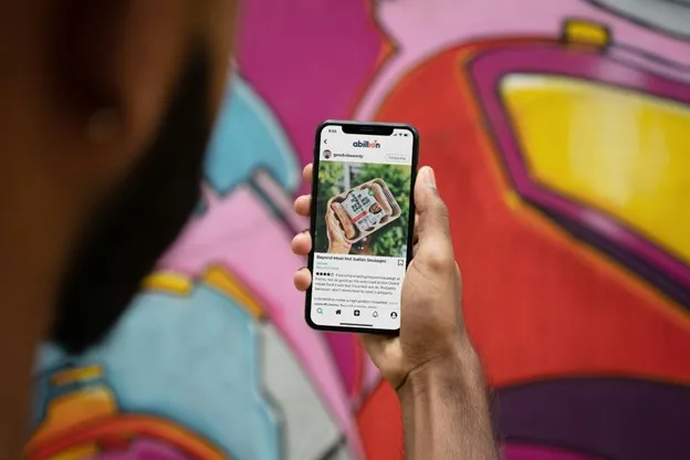 A person holds a smartphone displaying post about vegan sausages in front of a colorful graffiti wall.