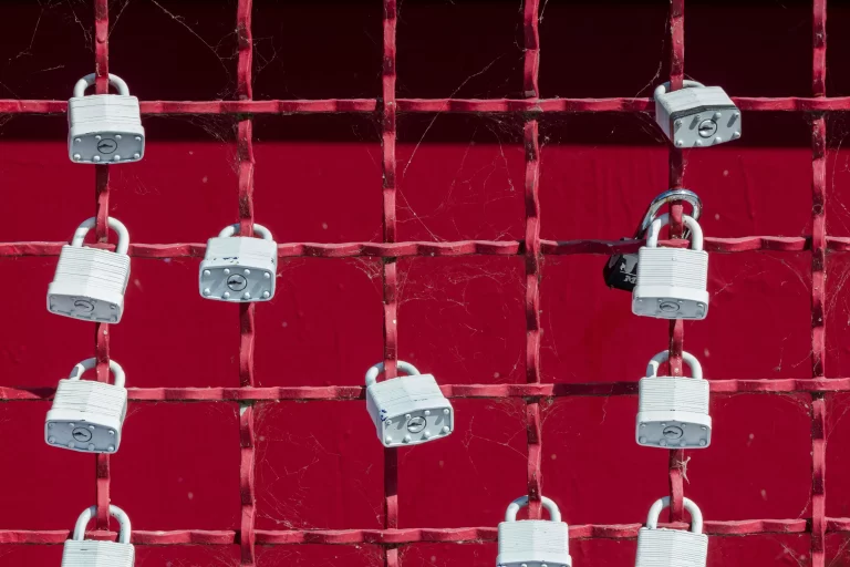 A red gate with numerous white locks attached.